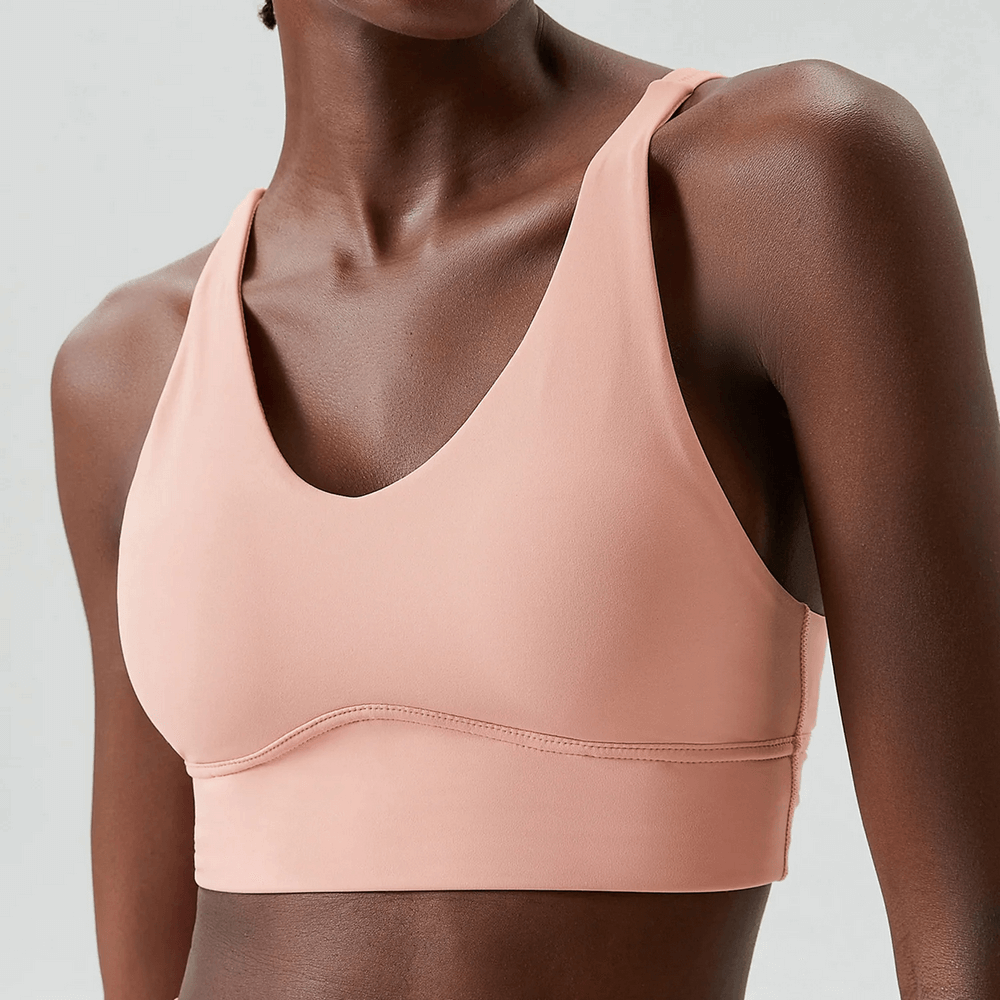 Woman wearing vibrant pink sports bra with crisscross back design, perfect for workouts. Model shows side view.